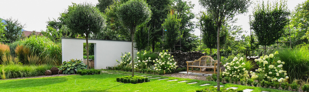Wunderschöner Garten mit grünem Rasen, Bäume und einer Gartenbank. | © Adobe Stock 284379076