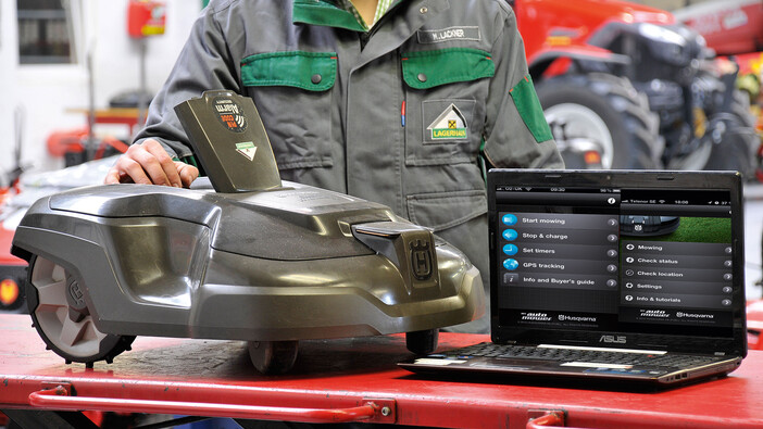 Auf dem Bild sieht man einen Rasenroboter beim Service und wie er mit einem Laptop verbunden ist.