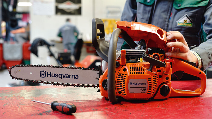 Auf dem Bild sieht man eine Husqvarna Motorsäge beim Servie und wie gerade das Gehäuse mit einem Schraubenzieher heruntergeschraubt wird.